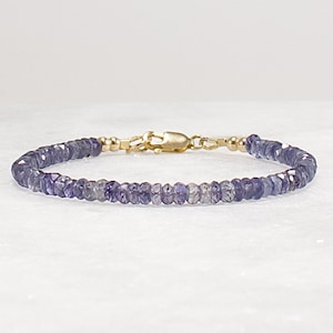 May include: A delicate bracelet made with small, faceted amethyst beads and a gold clasp. The bracelet is a light purple color and has a simple, elegant design.