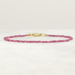 May include: A delicate pink gemstone bracelet with a gold clasp. The bracelet is made of small, round beads and is perfect for everyday wear.