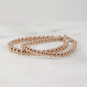May include: Two rose gold beaded bracelets with a clasp closure. The bracelets are stacked on top of each other.
