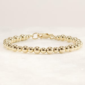 May include: A gold beaded bracelet with a clasp closure. The bracelet is made of small, round beads.