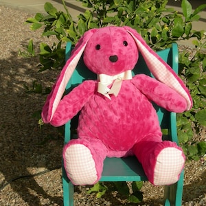 May include: A large, plush pink bunny rabbit with long ears and a white bow tie. The bunny has a black nose and eyes. The inside of the ears and the soles of the feet are patterned with a pink and white gingham check. The bunny is sitting on a teal chair.