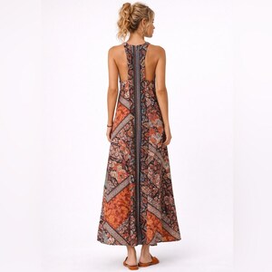 Könnte beinhalten: Ein langes, gemustertes Kleid mit Neckholder-Ausschnitt. Das Kleid hat eine Mischung aus warmen Farben, darunter Orange, Braun und Rot, mit floralen und geometrischen Mustern. Das Kleid ist bodenlang und hat eine lockere Passform, geeignet für Freizeitkleidung.