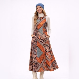 Puede incluir: Un vestido largo sin mangas con un patrón de retazos de estampados florales y geométricos en naranja, negro y azul, usado sobre una camisa de cuello alto color crema de manga larga, junto con un gorro azul y botas de color claro.