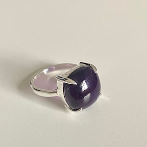 Op de afbeelding: Een zilveren ring met een grote, donkerpaarse edelsteen in een klauwsetting.