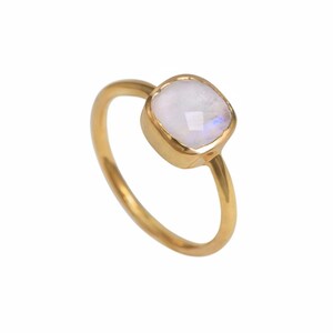 May include: A gold ring with a square moonstone gemstone. The moonstone has an iridescent quality and is set in a gold bezel. The ring's band is plain, polished gold. The background is white.