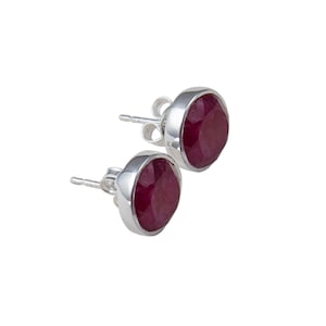 May include: A pair of silver stud earrings with red gemstone accents. The gemstones are faceted and have a round shape.