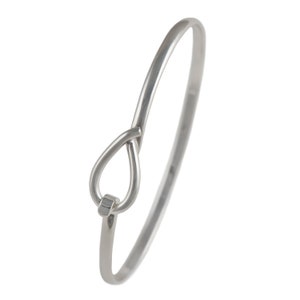 May include: A silver-colored bangle bracelet with a unique teardrop-shaped design at the clasp. The bracelet has a smooth, polished finish and a simple, elegant style. The clasp is a small, rectangular shape.