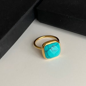 May include: A gold ring with a turquoise gemstone. The gemstone is a square shape with a faceted cut.