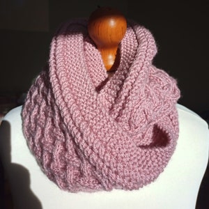 May include: A pink knitted infinity scarf with a cable knit pattern.