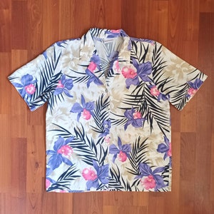May include: A white button-up shirt with a tropical print featuring large purple and pink flowers and dark green leaves.