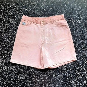 Pode incluir: Um par de calções de ganga rosa claro com um aspeto desbotado. Os calções têm cintura alta e um ajuste descontraído.