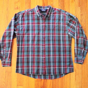 Puede incluir: Una camisa de cuadros de manga larga con cuello y puños abotonados. El diseño de cuadros incorpora líneas turquesa, burdeos, negras y blancas. La camisa está hecha de una tela suave y tejida.