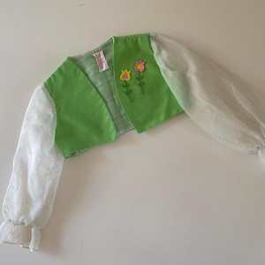 May include: A green bolero jacket with sheer white sleeves. The jacket features embroidered flowers and a ruffled cuff. The bolero is a light green color with a plaid lining.