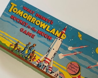 Puede incluir: Caja de juego vintage de Walt Disney's Tomorrowland Rocket to the Moon. La caja presenta una ilustración de cohete con rayas rojas y blancas y un fondo de cielo azul. La caja tiene el texto "Next rocket flight in 5 minutes."