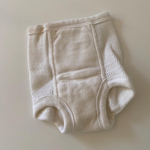 May include: A white cotton training pant with a textured design. The pant has a built-in absorbent pad.