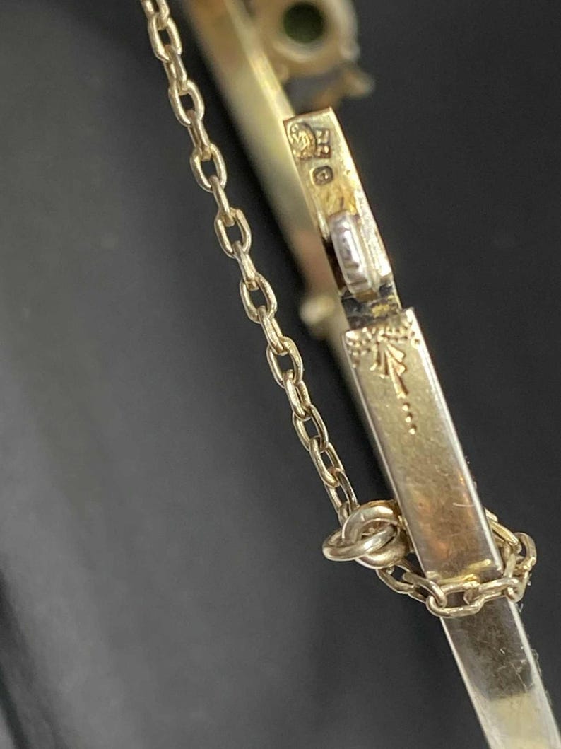 Puede incluir: Primer plano de una pulsera dorada con una delicada cadena y cierre. La pulsera presenta detalles y marcas intrincadas, lo que sugiere que es vintage o antigua. El fondo oscuro resalta la joya.