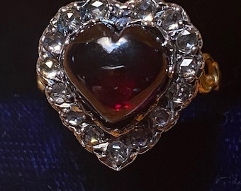 May include: A heart-shaped ring with a red gemstone surrounded by a halo of small diamonds.