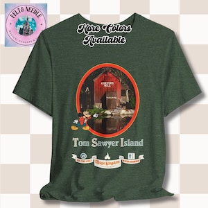 May include: Dark green t-shirt featuring a circular graphic of a red building with the text "Harpers Mill" and Mickey Mouse. The shirt also has the text "Tom Sawyer Island" and "Magic Kingdom". The words "More Colors Available" are at the top.