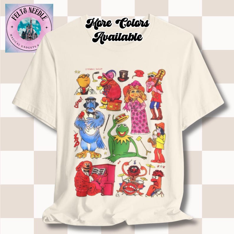 May include: White t-shirt featuring a colourful graphic print of characters from the Muppets. The characters include Kermit the Frog, Miss Piggy, Animal, and Gonzo. The text "More Colors Available" is printed at the top of the shirt.