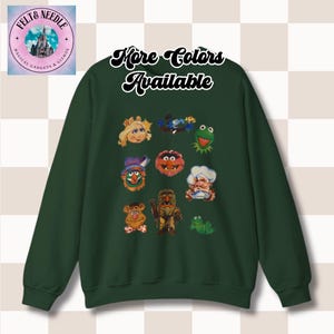 Puede incluir: Una sudadera verde oscuro con un estampado gráfico de personajes de Plaza Sésamo. El texto "More Colors Available" está impreso en la parte delantera de la sudadera.