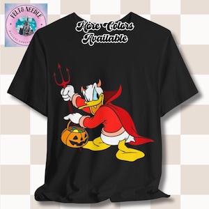 以下が含まれることがあります： 黒いTシャツ。悪魔の格好をしたドナルドダックの漫画が描かれており、三叉とカボチャのバケツを持っています。シャツには「More Colors Available」の文字。左上にロゴがあります。ハロウィーンに最適です。