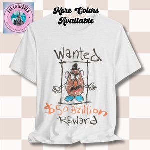 Peut inclure: T-shirt blanc avec une illustration de style dessinée à la main d'un personnage de pomme de terre avec le mot "Wanted" au-dessus. Le texte "$50 Bzillion REWARD" est écrit en dessous du personnage. Le t-shirt porte également le texte "More Colors Available".
