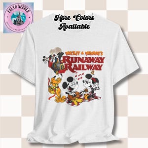 Puede incluir: Camiseta blanca con un gráfico colorido de Mickey y Minnie Mouse, Pluto y un tren, con el texto "Mickey & Minnie's Runaway Railway." La camiseta también tiene el texto "More Colors Available."