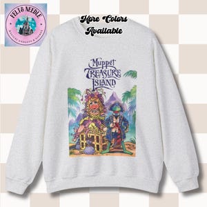 May include: A light grey sweatshirt with a colourful graphic from Muppet Treasure Island. The design features two Muppet characters, a treasure chest, and the text "Muppet Treasure Island". The sweatshirt also has the text "More Colors Available".