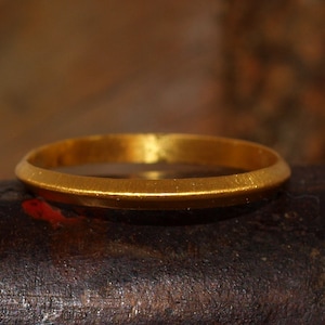 May include: A simple gold band ring with a smooth, slightly rounded surface.