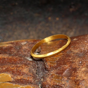 May include: A simple gold band ring, with a slightly hammered finish, resting on a piece of weathered wood.