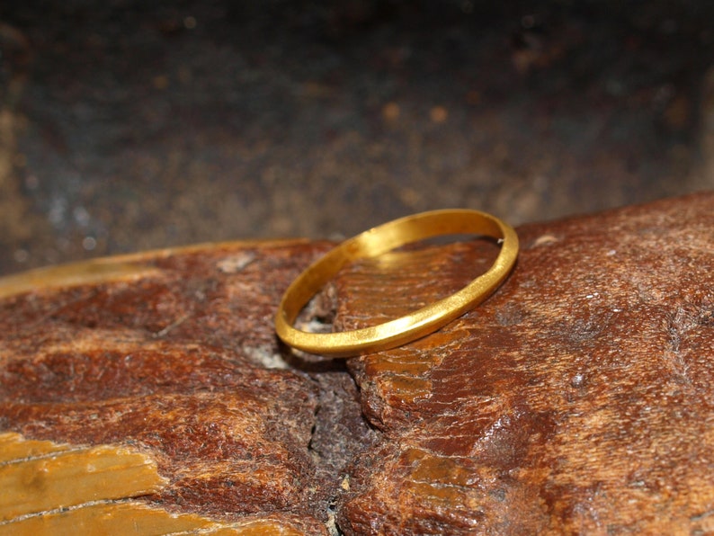 May include: A simple gold band ring, with a slightly hammered finish, resting on a piece of weathered wood.