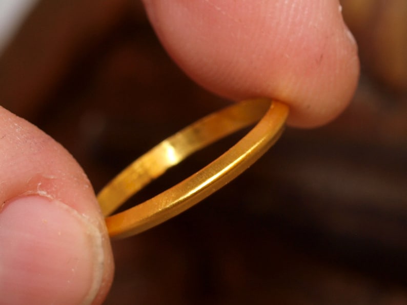 May include: A simple gold band ring, held between two fingers.