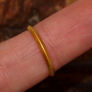 May include: A simple gold band ring worn on a finger.