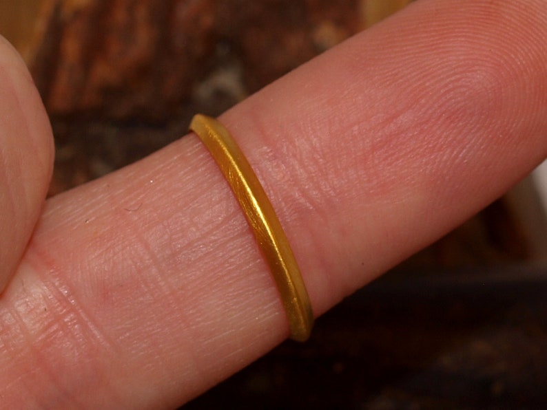 May include: A simple gold band ring worn on a finger.