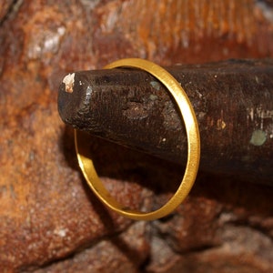 May include: A thin gold band ring is placed on a wooden ring mandrel.