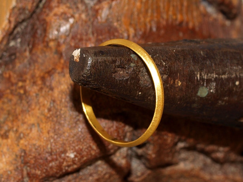 May include: A thin gold band ring is placed on a wooden ring mandrel.