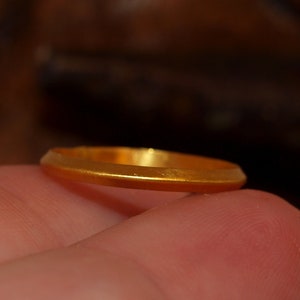 May include: A simple gold band ring, shown on a finger.