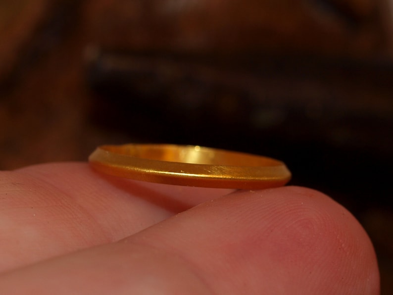 May include: A simple gold band ring, shown on a finger.