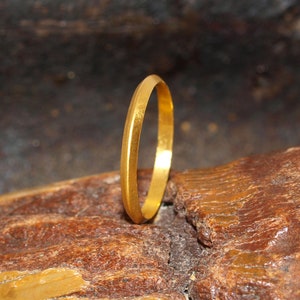 May include: A simple gold band ring, shown on a textured brown surface.