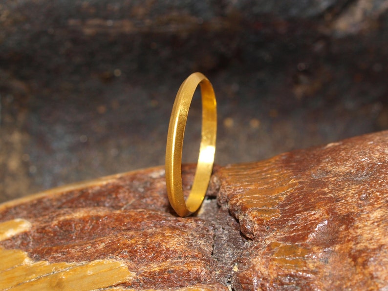 May include: A simple gold band ring, shown on a textured brown surface.