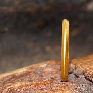May include: A gold band ring with a faceted, hexagonal design. The ring is sitting on a piece of wood.