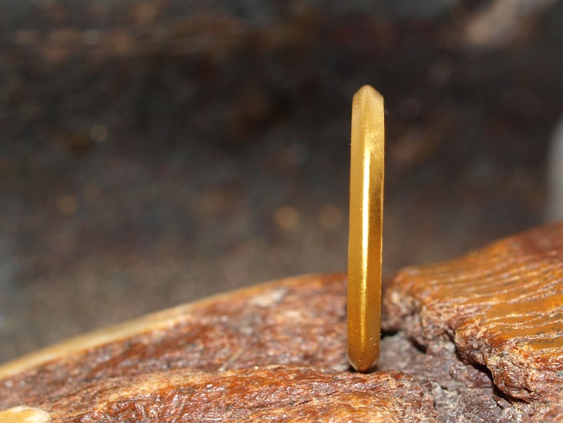 May include: A gold band ring with a faceted, hexagonal design. The ring is sitting on a piece of wood.