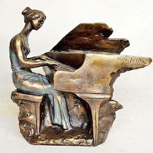 Può includere: Una scultura in bronzo di una donna che suona il pianoforte. La scultura è dettagliata e realistica, con l'abito della donna e i tasti del pianoforte chiaramente visibili. La scultura è firmata "Luis Jordá" sul pianoforte.