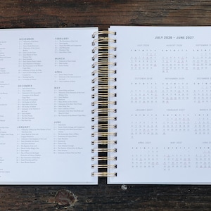 Peut inclure: Agenda ouvert avec des pages blanches et une reliure spirale dor&eacute;e. La page de gauche r&eacute;pertorie les mois avec les dates, tandis que la page de droite affiche un calendrier de juillet 2020 &agrave; juin 2021. L'agenda est ouvert sur une surface en bois fonc&eacute;.