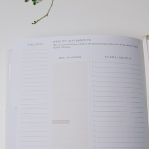 Peut inclure: Un planificateur ouvert avec des sections pour les courses, la planification des repas et les listes de t&acirc;ches. La semaine du 28 septembre est not&eacute;e, avec une citation de Th&eacute;r&egrave;se de Lisieux. Une branche de plantes vertes est dans le coin sup&eacute;rieur gauche.