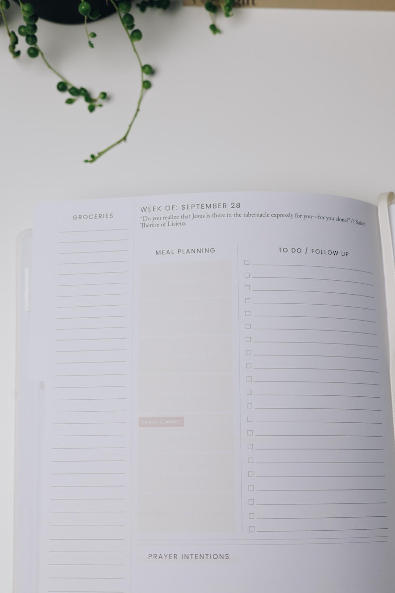 Peut inclure: Un planificateur ouvert avec des sections pour les courses, la planification des repas et les listes de t&acirc;ches. La semaine du 28 septembre est not&eacute;e, avec une citation de Th&eacute;r&egrave;se de Lisieux. Une branche de plantes vertes est dans le coin sup&eacute;rieur gauche.
