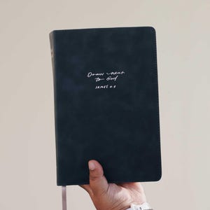 May include: A dark blue book with the handwritten text "Draw near to God" and "JAMES 4:8". The book has a pink ribbon bookmark.