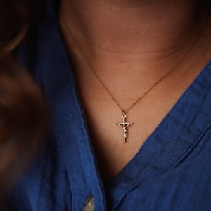 Op de afbeelding: Goudkleurige kruis-hangerketting. Het kruis heeft een gedetailleerde afbeelding van Jezus Christus. De ketting wordt gedragen over een blauw overhemd.