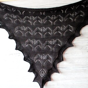 K&ouml;nnte beinhalten: Ein schwarzer gestrickter Schal mit einem Spitzenmuster aus Flederm&auml;usen. Der Schal ist dreieckig und hat einen gewellten Rand.