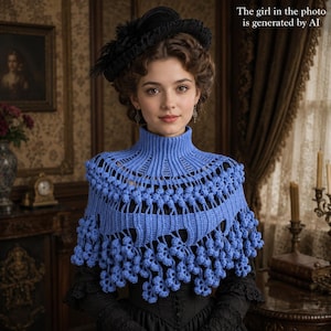 May include: A bright blue crochet capelet featuring a high ribbed collar and an intricate openwork pattern adorned with numerous small, dangling bobble clusters along the hemline. The garment is worn over a black long-sleeved top.